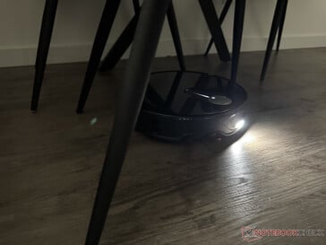 O Roborock Qrevo Slim com sua luz acesa no labirinto de pernas da cadeira